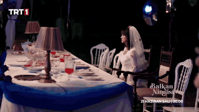a woman in a wedding dress sits at a long table with trt1 on the bottom left