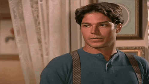 a man wearing suspenders and a blue shirt stands in front of a picture