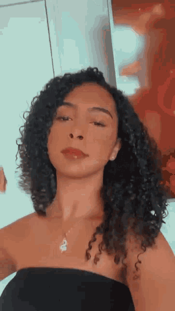 a woman with curly hair is taking a selfie while wearing a black top .