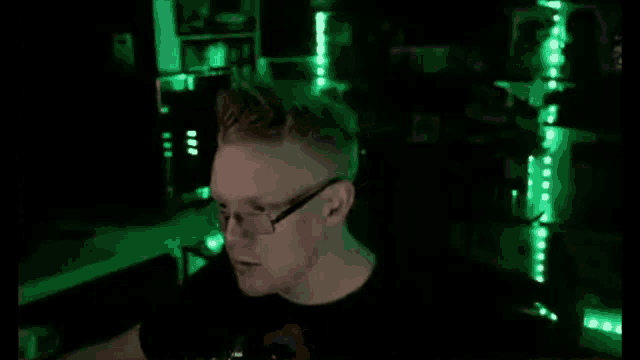 a man wearing glasses is sitting in a dark room with green lights .