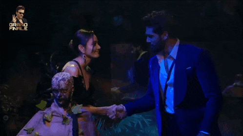 a man in a blue suit is standing next to a woman in a black dress in a dark room with the words grand finale behind them