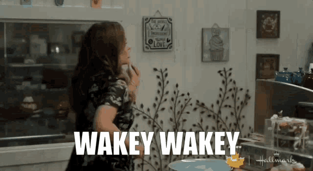 a woman is standing in a kitchen with the words wakey wakey on the wall behind her .