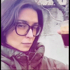 a woman wearing glasses and a jacket holds a cup of coffee