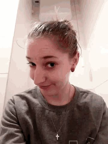 a woman wearing a necklace with a cross on it is taking a selfie in a bathroom .