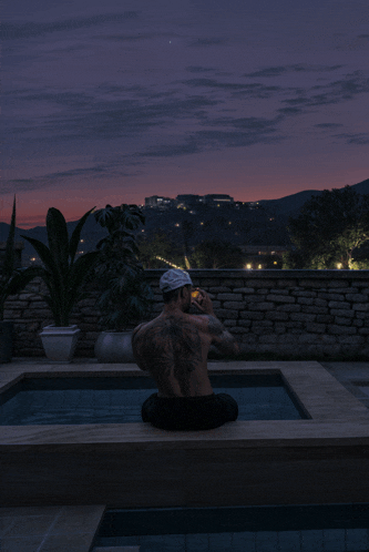 a man with a tattoo on his back is sitting in a pool at night
