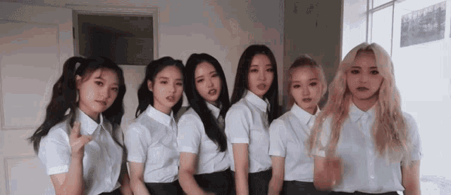 a group of girls are standing next to each other in a room wearing white shirts and skirts .