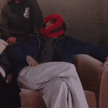 a man wearing a blue jacket and a red fur hat sits on a couch