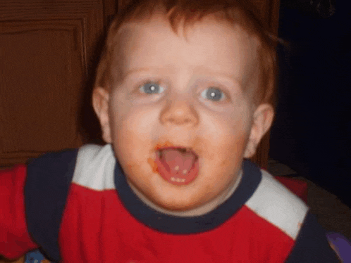 a young boy with his tongue hanging out is wearing a red and white shirt