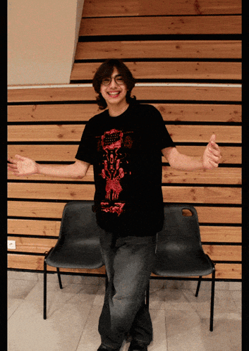 a man wearing a black shirt with a red design on it is standing in front of a wooden wall