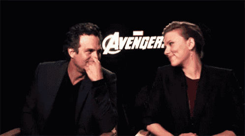 a man and a woman are sitting in front of a sign that says ' avengers '