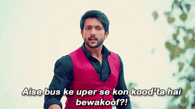 a man in a red vest and black shirt says aise bus ke uper se kon kood ' ta hai bewakoor ?