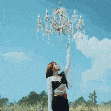 a woman stands in front of a tree with flowers and a chandelier