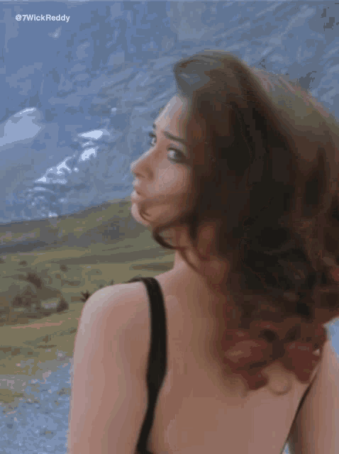 a woman in a black tank top is standing in front of mountains