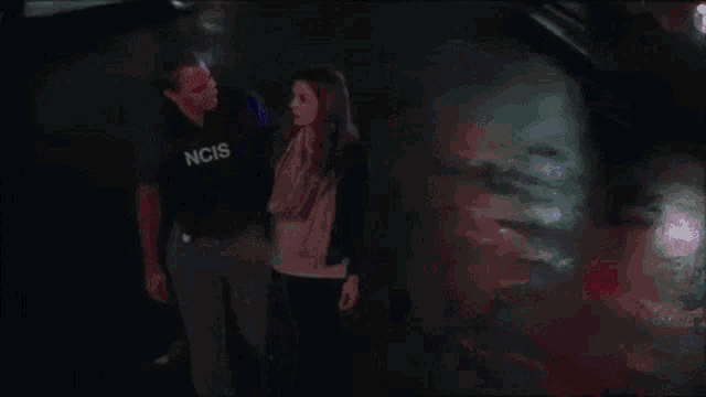 a man in a ncis uniform leads a woman down a street