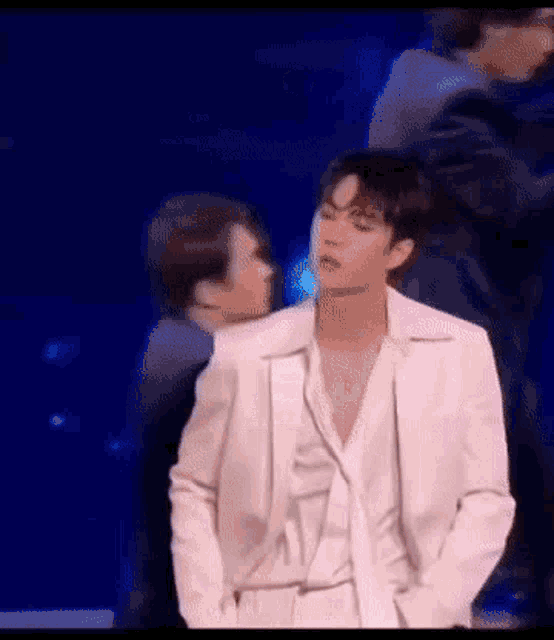 a man in a white suit is standing on a stage with other people .