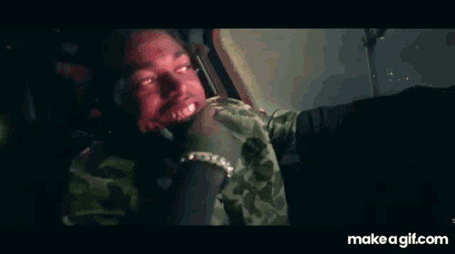 a man in a camouflage shirt is sitting in a car with his mouth open .