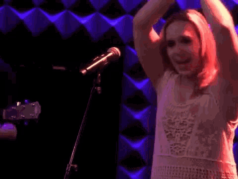 a naked woman singing into a microphone in front of a checkered wall