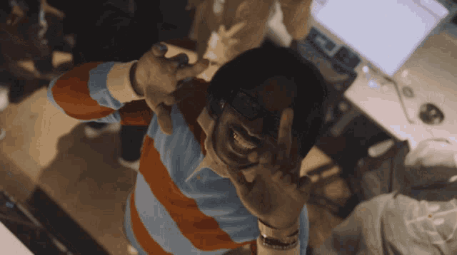 a man wearing glasses and a striped shirt is smiling and making a peace sign