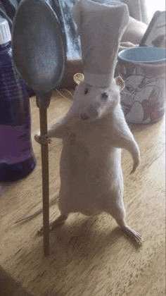 a stuffed rat wearing a chef 's hat is holding a spoon on a table .