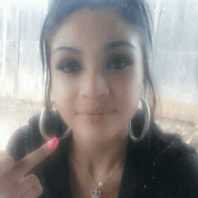 a woman wearing hoop earrings and a necklace is making a funny face and giving the middle finger .