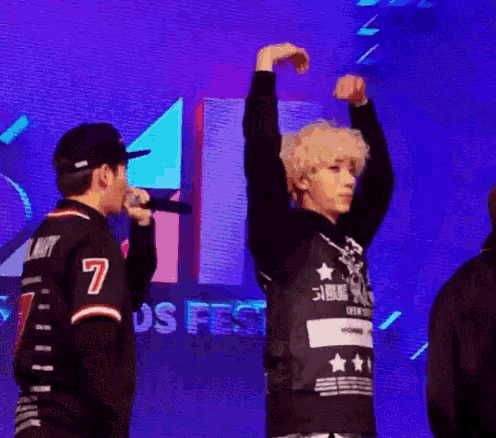 a man is singing into a microphone while another man holds his hands in the air .
