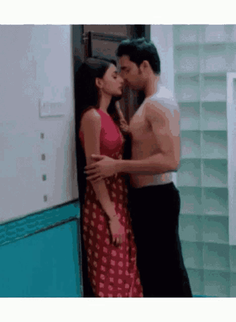 a man without a shirt is kissing a woman in a red saree .