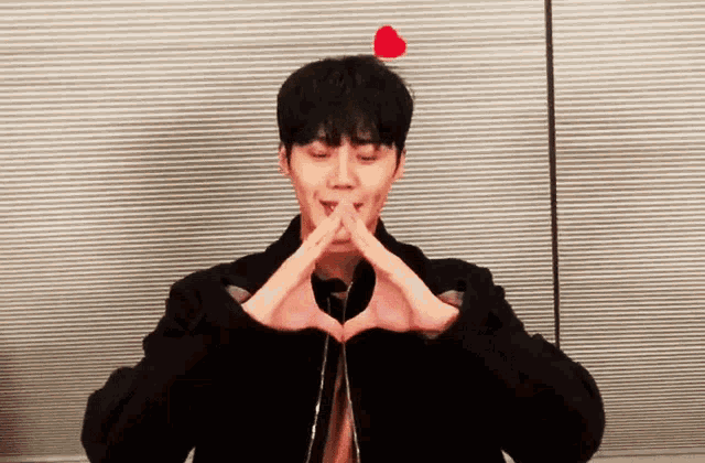 a man in a black jacket making a heart shape with his hands