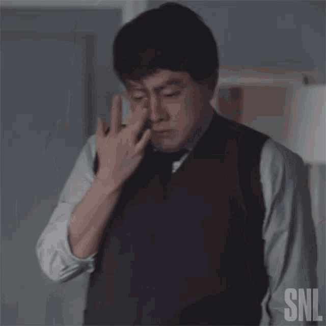 a man in a suit and tie is covering his eyes with his finger .
