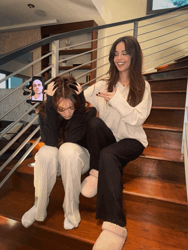 two women are sitting on a set of stairs with one holding a picture of a man