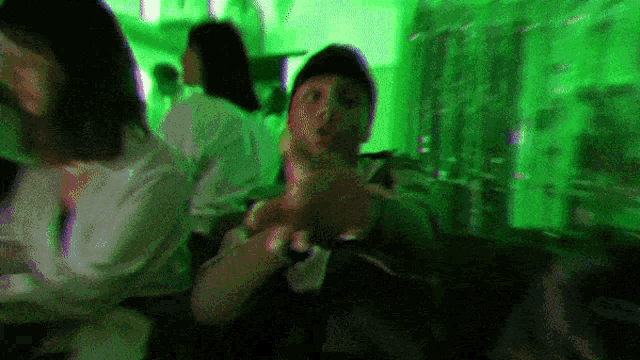 a group of people are sitting in a dark room with a green light behind them