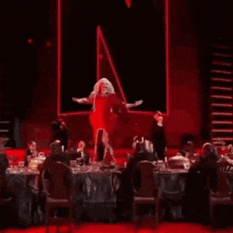 a drag queen in a red dress is dancing on a stage with her arms outstretched .