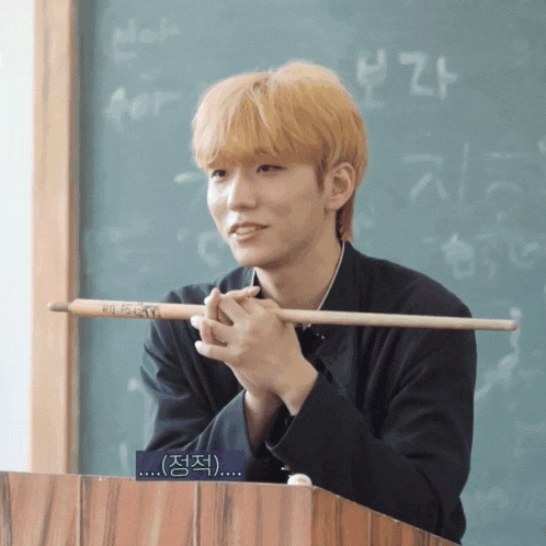a young man holds a drum stick in front of a blackboard with foreign writing on it