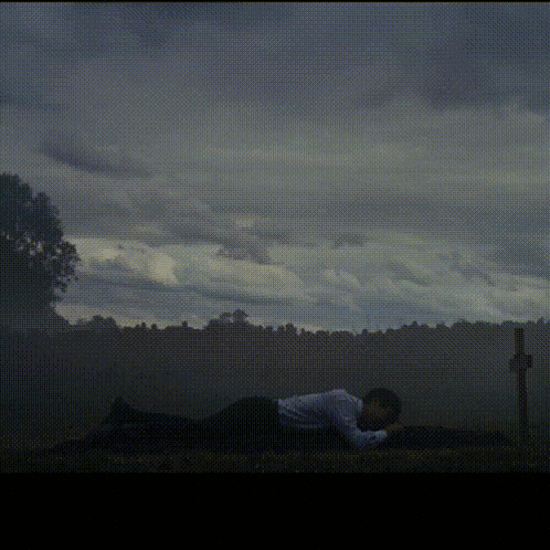 a man is laying on the ground in front of a cross