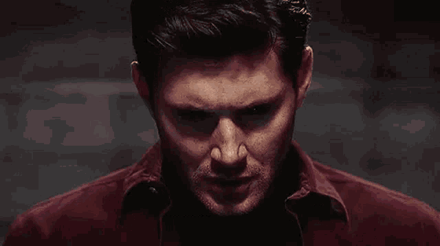 a close up of a man 's face with black eyes and a red shirt .