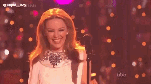 a woman is laughing and clapping on a stage while holding a microphone .