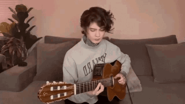 a person sitting on a couch playing a guitar and wearing a sweater that says oakim