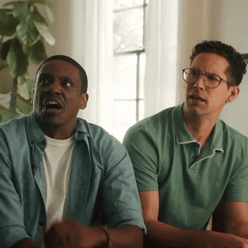 two men sitting next to each other one wearing glasses and a blue shirt