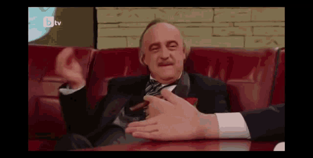 a man in a suit and tie is sitting on a red couch with btv written on the bottom left
