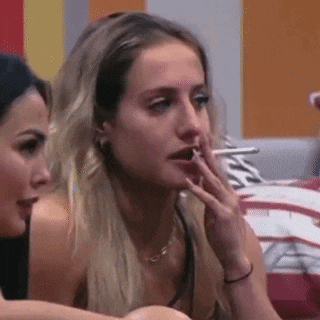 a woman is smoking a cigarette while sitting next to another woman on a bed .