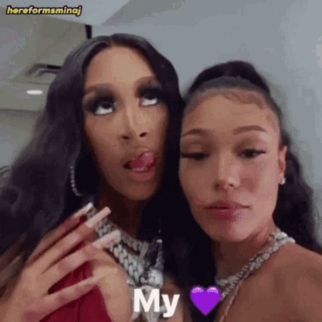 two women are standing next to each other and one of them is sticking her tongue out and the other is holding a purple heart .