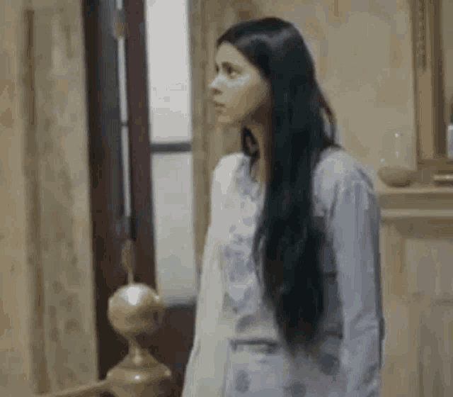 a woman with long black hair is standing in a room in front of a mirror .
