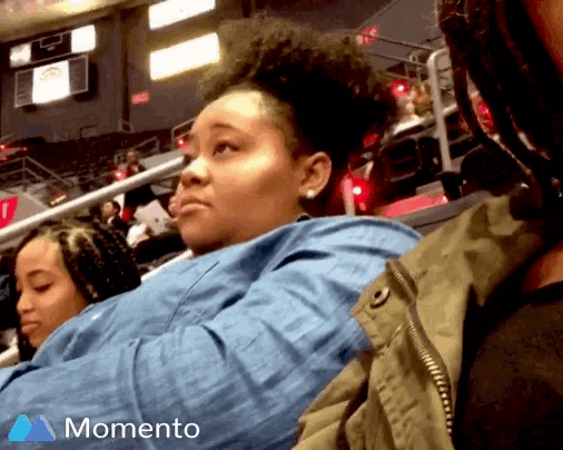 a woman sitting in a stadium with a momento logo on the bottom