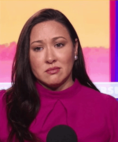 a woman in a pink shirt is sitting in front of a microphone with a sad look on her face .