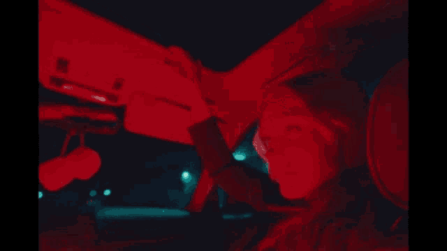 a woman is sitting in a car with a red light on her face