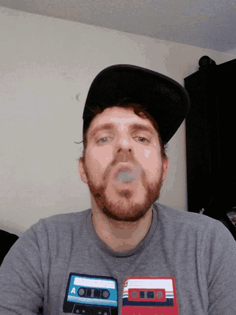 a man with a beard is wearing a hat and a shirt with a cassette tape on it