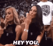 two cheerleaders are sitting in the stands at a basketball game and blowing kisses .