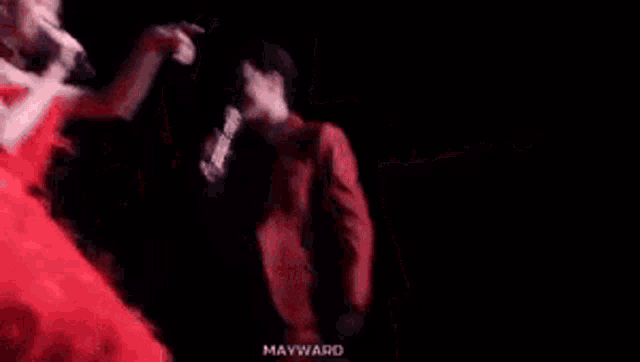 a man and woman are singing into microphones on a stage . the woman is wearing a red dress .