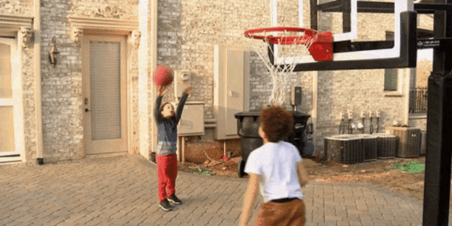 two young boys playing basketball in front of a brick building