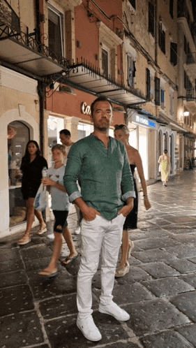a man in a green shirt and white pants stands in front of a building that says optical