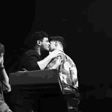 a black and white photo of two men kissing in a dark room